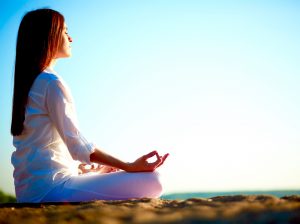 Side view of meditating woman sitting in pose of lotus against blue sky outdoors